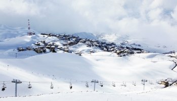 Winter mountain ski resort landscape with snow and cute little houses, chairlift with people playing sport