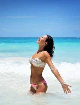 Happy joyful girl standing in a water and enjoying bright sunny day, sexy model with pleasure spending summer vacation on Caribbean Sea, Cancun, Mexico, North America