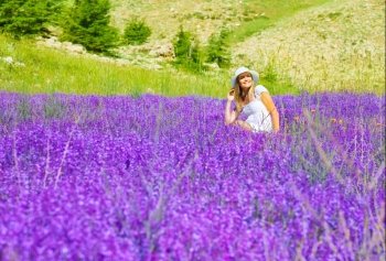Beautiful woman on lavender meadow, pretty smiling girl sitting on floral field, cute happy female enjoying purple flowers, cheerful teenager relaxed outdoors, natural beauty, summer holiday concept