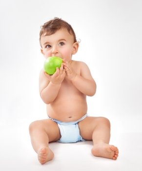 Cute little baby boy sitting in the studio over white background and eating fresh green apple, happy healthy childhood