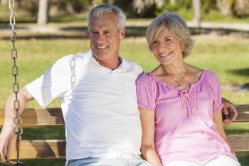 Happy senior man and woman couple sitting together on a park bench outside in sunshine