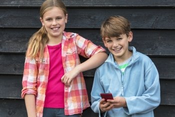 Two children boy and girl smiling and using cell phone