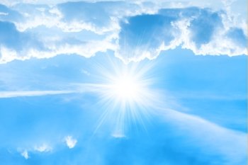 Big bright sun with sunrays on white clouds and blue sky
