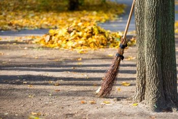 Cleaning in the autumn park - broom with pile of yellow fallen leaves