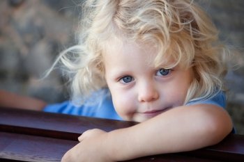 Little child three year old with blond curly hair hidden behind a wooden bench
