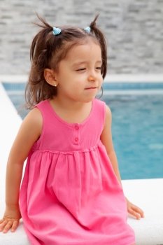 Funny little girl with pigtails sitting near the pool