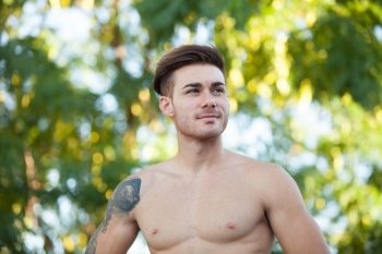 Handsome fit athletic shirtless young man against green nature