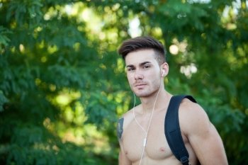 Handsome shirtless young man doing hiking while listening to music