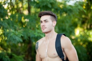 Handsome shirtless young man doing hiking while listening to music