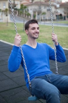 Young cool men dressed in blue in the park sitting on a swing