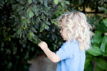 Beautiful boy three year old with long blond hair near of a tree