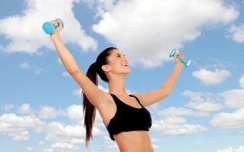 Happy brunette woman toning her muscles on a bluy sky of background