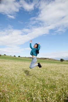 Young brunette girl jumping in a field full of flowers
