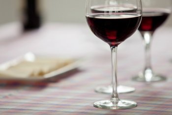 Glasses of red wine and cheese tray on a table with checkered tablecloth