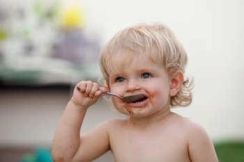 Funny blond baby eating chocolate with a spoon