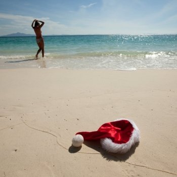 Christmas hat on beach. Closeup christmas hat on a white stropical sandy sea beach ans woman in bikini