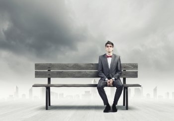 Businessman on bench. Young businessman in red glasses sitting on bench