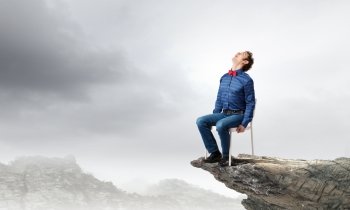 Man on top. Emotional businessman sitting in chair on top of mountain
