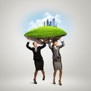 Challenge in business. Image of two businesswomen holding lawn above head. Partnership and ecology