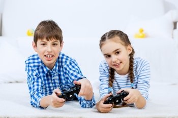 Kids playing game console. Cute kids lying on floor playing games on joystick