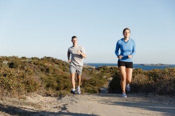 Sport runner jogging on beach working out with her partner. Fit female fitness model jogging along ocean with her partner