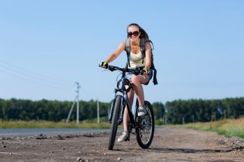 Your active lifestyle position. Young sporty girl with backpack riding bicycle along roadside