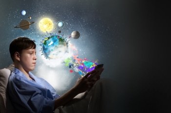 Surfing internet before sleep. Teenage boy in pajamas lying in bed using tablet pc. Elements of this image are furnished by NASA