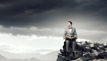 Businessman reading old book. Young handsome businessman on rock edge with old book in hands