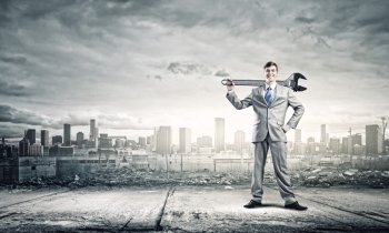 Working mechanism. Young businessman with wrench against city background