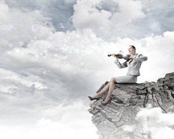 Woman violinist. Young businesswoman sitting on rock and playing violin
