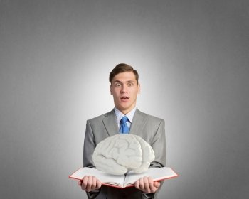 Book to broaden your mind. Shocked businessman holding opened book with brain picture