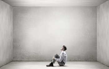 Businessman in isolation. Young depressed businessman sitting on floor alone in empty room