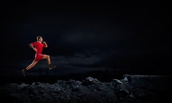 At full speed. Running man in red sport wear on dark background