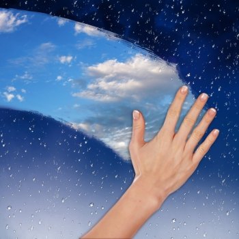 Hand cleaning window with blue sky and white clouds
