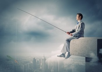Fishing concept. Businessman sitting on top of building and fishing with rod