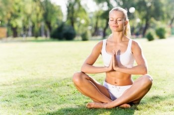 Yoga practice. Young woman in white sitting on grass in lotus pose