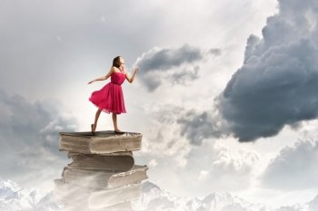 Education concept. Woman in red dress standing on pile of books