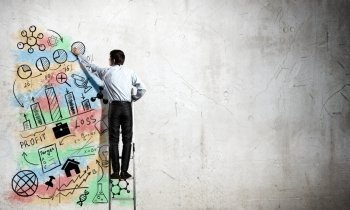 His bright strategy plan . Back view of businessman standing on ladder and drawing on wall