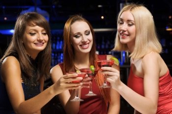 Weekend party. Three elegant ladies with cocktails at night club