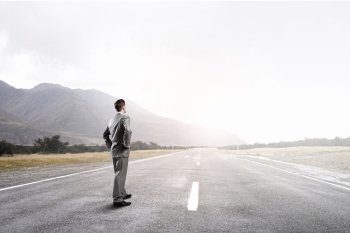 Businessman choosing his way. Young businessman with arms on waist standing on asphalt road