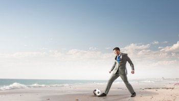Businessman kicking ball. Young businessman in suit playing football at ocean coast