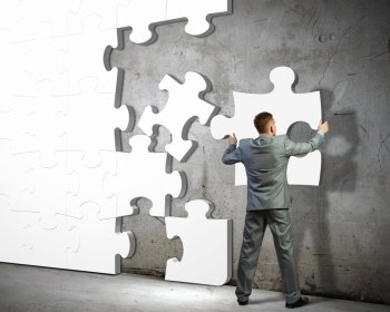 Problem solving. Image of businessman compiling macro white puzzle. Building business
