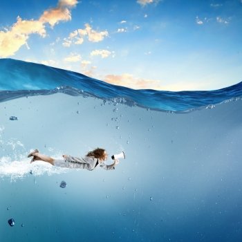 Businesswoman under water. Young businesswoman in suit swimming in crystal blue water