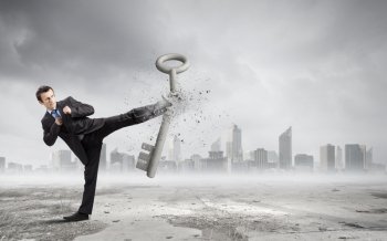Key to success. Angry businessman crashing stone key with kick