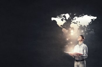 Guy with glowing book. Young businessman with opened book in hands and world map on background