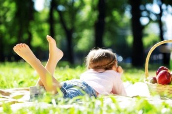 Child lying on blanket having picnic in summer park. Girl in park