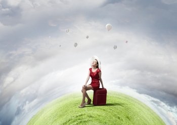 Woman in red. Young woman in red dress on road sitting on her red luggage