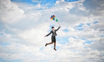 Woman flying in sky. Young businesswoman in suit and bowler hat flying on windmill