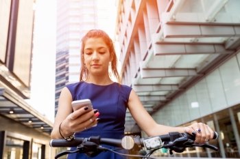 Young woman commuting on bicycle. Young woman in business wear on bicycle and holding mobile phone