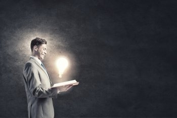Broaden your mind. Businessman holding opened book with glass glowing light bulb 